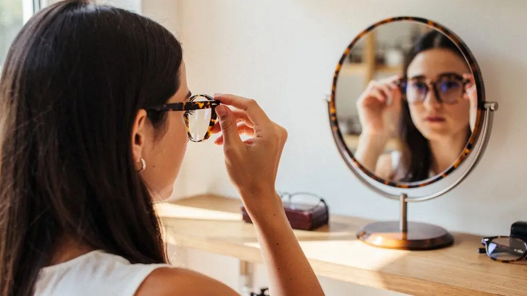 Une cliente observe le reflet d'une monture brillante dans un miroir chez un opticien.