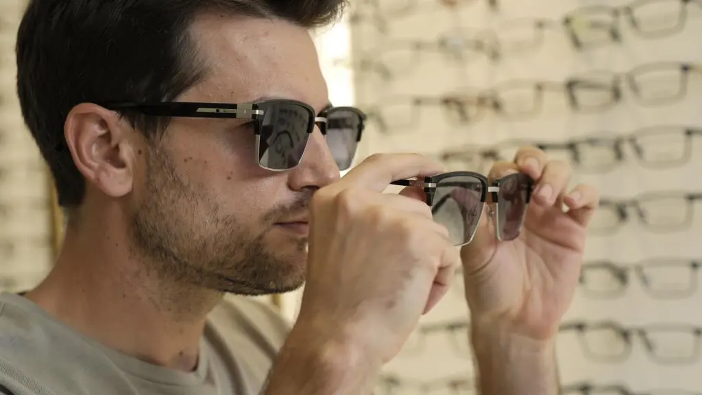 Un homme compare deux paires de lunettes rectangulaires devant une présentation en magasin.